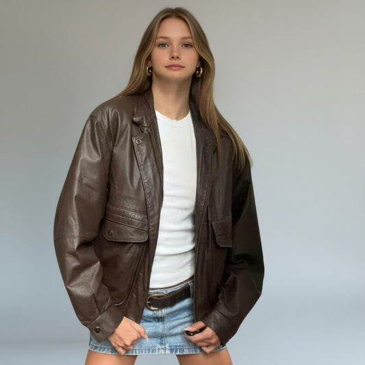Woman wearing a brown leather jacket over a white shirt and denim skirt on a plain background