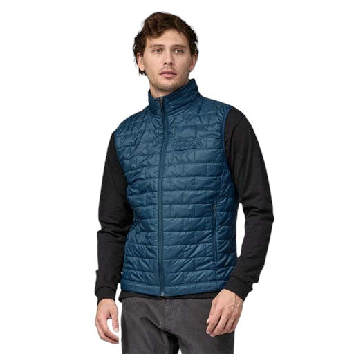 A man wearing a blue quilted vest over a black shirt paired with gray trousers.