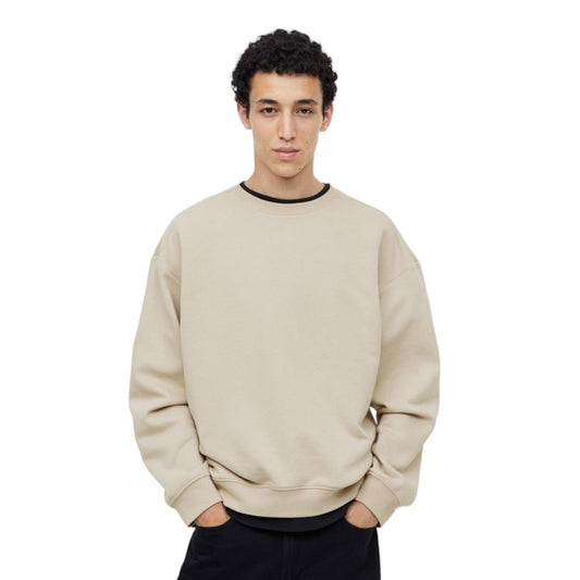 Man wearing a beige sweatshirt and black pants on a white background