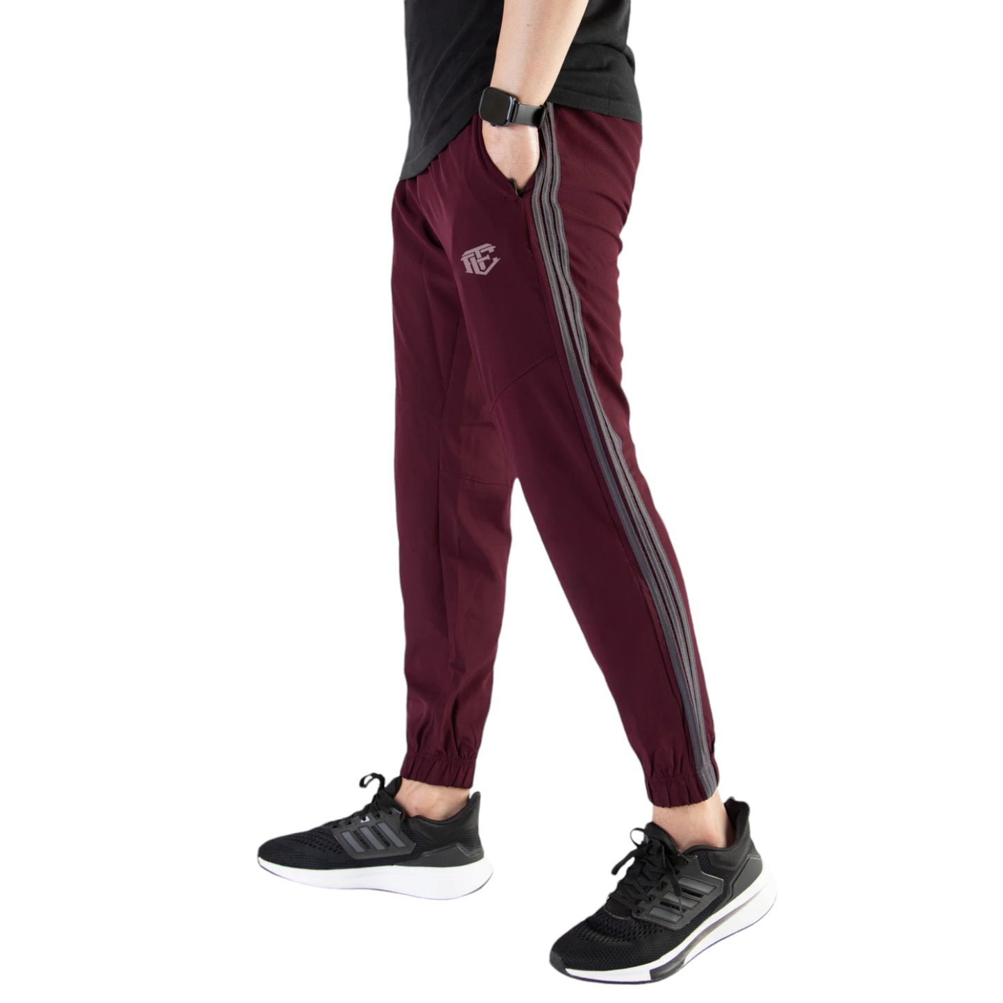 A person wearing maroon trousers with three gray stripes on the side, paired with a black shirt and black sneakers.