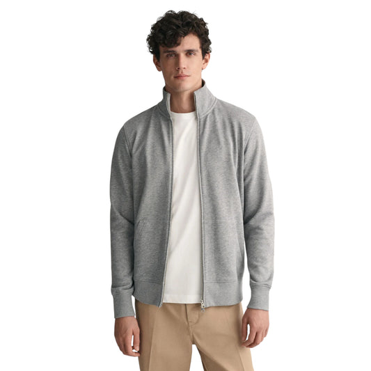 A man wearing a full-zip high collar grey jacket with a white t-shirt underneath and beige pants.