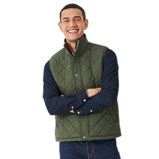A man wearing a quilted olive green vest with a stand collar, paired with a navy blue shirt and blue jeans.