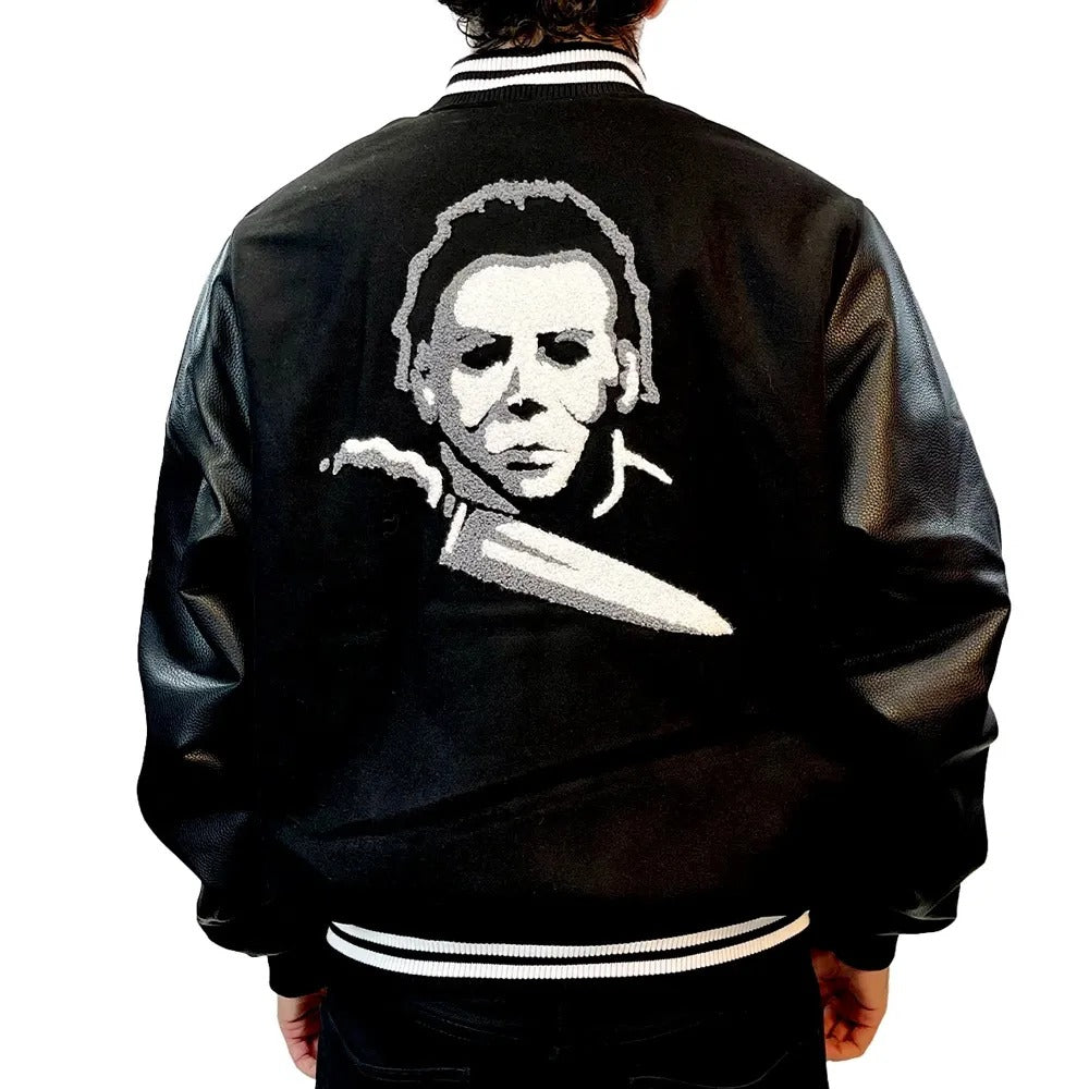 Black letterman jacket with a white graphic of a face and knife on the back, worn by a person.