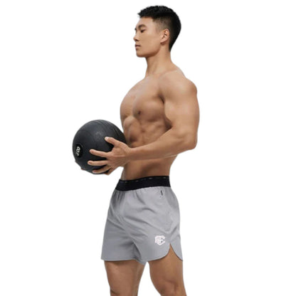 Man holding a medicine ball wearing gray shorts with a logo on a white background