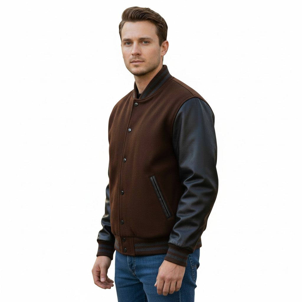 A man wearing a brown and black varsity-style jacket with dark brown wool body and black leather sleeves, paired with blue jeans, against a plain white background.