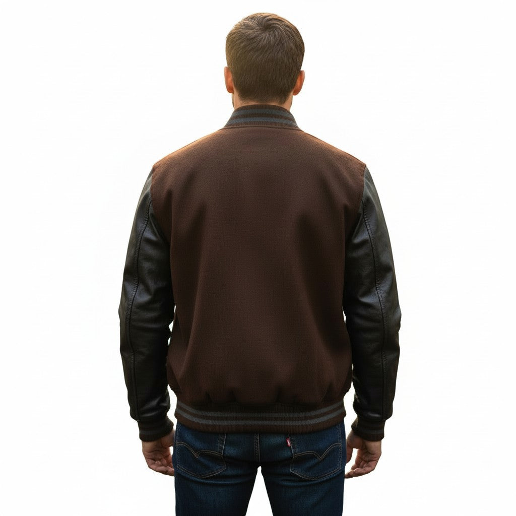 A man viewed from behind wearing a brown and black leather-look varsity jacket with dark blue jeans, set against a plain white background.