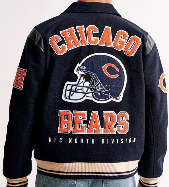 Chicago Bears navy blue varsity jacket shown from the back, featuring orange and white lettering, a large football helmet graphic, and ribbed beige and navy trim.