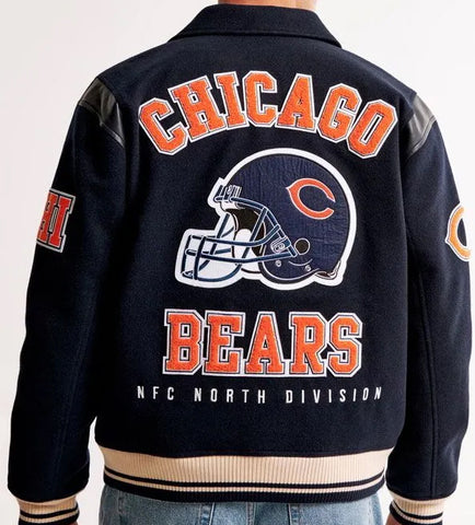 Chicago Bears navy blue varsity jacket shown from the back, featuring orange and white lettering, a large football helmet graphic, and ribbed beige and navy trim.