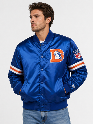A man wearing a blue satin jacket with Denver Broncos graphics, including a large 'D' logo on the chest and an NFL shield on the sleeve, photographed against a light gray studio background.