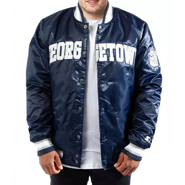 A man wearing a navy blue varsity jacket with 'GEORGETOWN' printed in white across the chest, layered over a white t-shirt. The jacket features a shiny satin-like finish, ribbed collar, cuffs, and hem, and a small embroidered logo on the left sleeve.