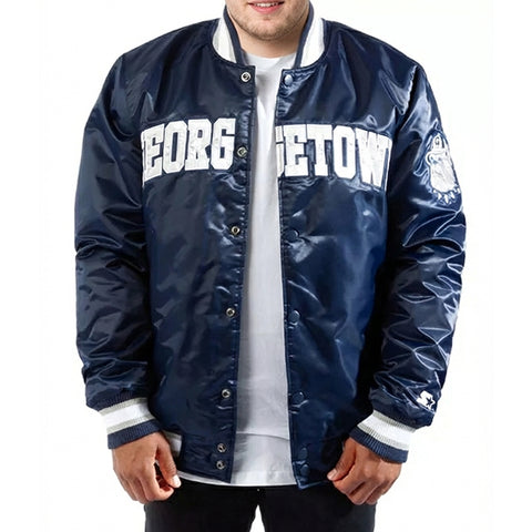 A man wearing a navy blue varsity jacket with 'GEORGETOWN' printed in white across the chest, layered over a white t-shirt. The jacket features a shiny satin-like finish, ribbed collar, cuffs, and hem, and a small embroidered logo on the left sleeve.