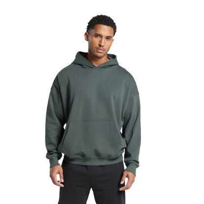 A male model wearing a green stacked fit hoodie with a kangaroo pocket, ribbed cuffs and hem, and an adjustable drawstring hood.