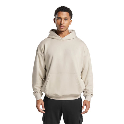 A man wearing a beige stacked hoodie with a kangaroo pocket, ribbed cuffs and an adjustable drawstring hood.