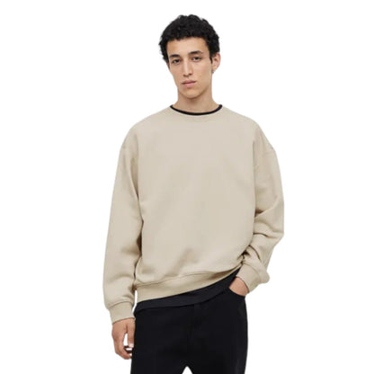 Person wearing a beige sweatshirt and black pants on a white background