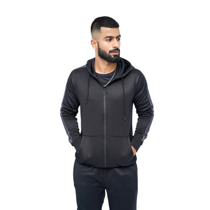 A man wearing a full-zip black windbreaker track jacket with side pockets and a hood.