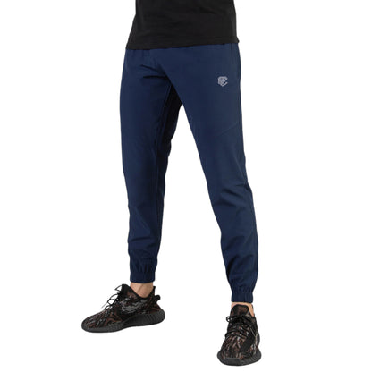 A male model wearing navy blue micro stretch tech pants with an elastic waistband and drawstring, featuring a slim fit and full length. The model is also wearing a black T-shirt and black sneakers.