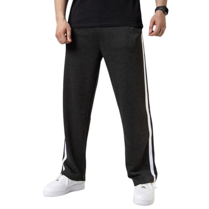 A person standing and facing forward, wearing black wide-leg trousers with two white stripes on the side, paired with a black T-shirt and white shoes.