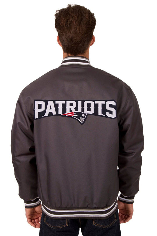 A man viewed from behind wearing a dark gray New England Patriots varsity jacket with 'PATRIOTS' and the team logo embroidered across the back.