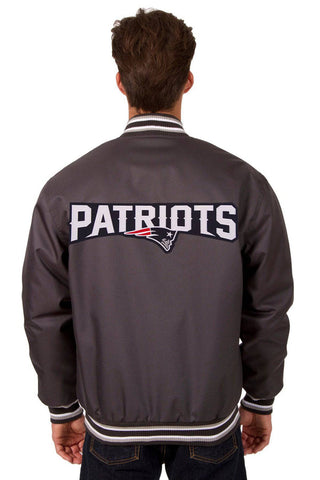 A man viewed from behind wearing a dark gray New England Patriots varsity jacket with 'PATRIOTS' and the team logo embroidered across the back.