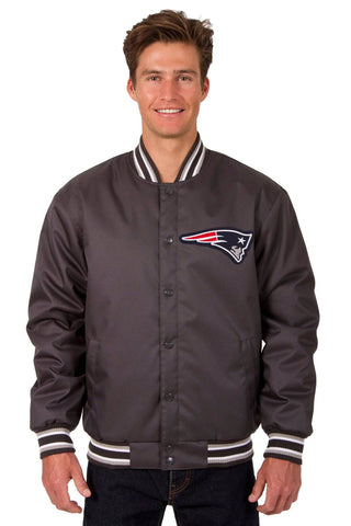 A man wearing a dark gray satin varsity jacket with the New England Patriots logo on the chest, featuring striped ribbed collar, cuffs, and hem, set against a plain white background.