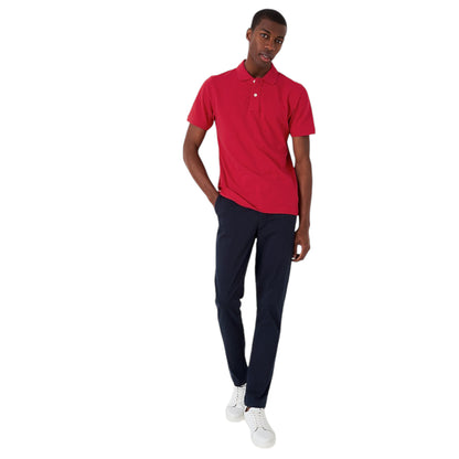 A man wearing a classic red polo shirt with a collar and short sleeves, paired with navy blue trousers and white sneakers.