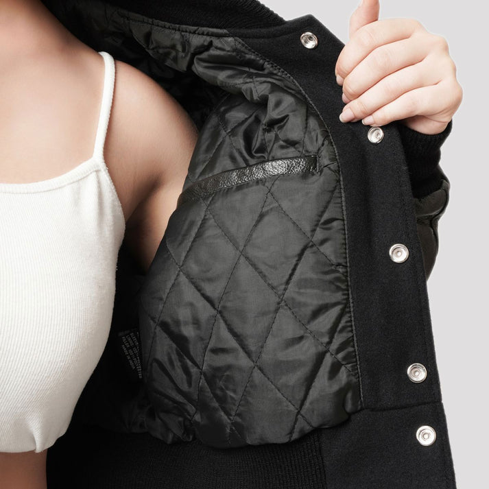 Close-up of a person wearing a black quilted jacket with silver snap buttons, holding the collar open to show the diamond-quilted black lining.