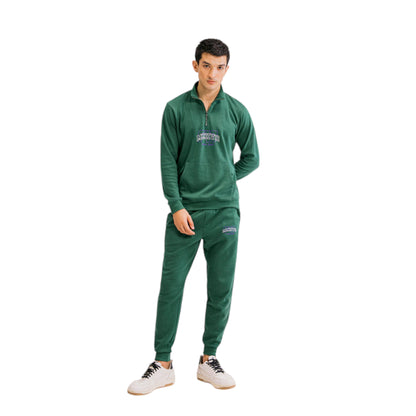 A man wearing a green half-zip tracksuit with a logo print on the chest and thigh, paired with white sneakers.