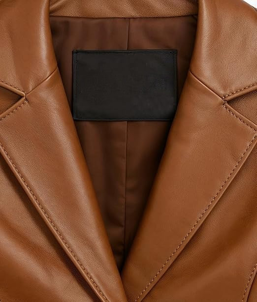 Close-up of a brown leather jacket with a black rectangular label patch inside the collar, showing the smooth texture and stitching details.
