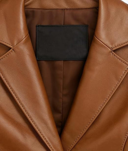 Close-up of a brown leather jacket with a black rectangular label patch inside the collar, showing the smooth texture and stitching details.