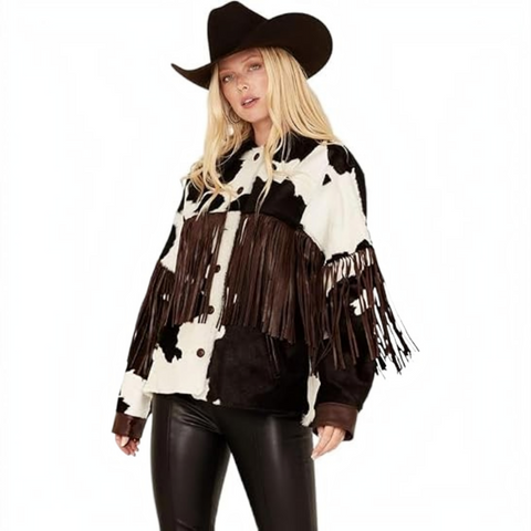 A woman modeling a black and white cow-print fringed jacket with a black cowboy hat and black faux-leather pants, set against a plain white background.
