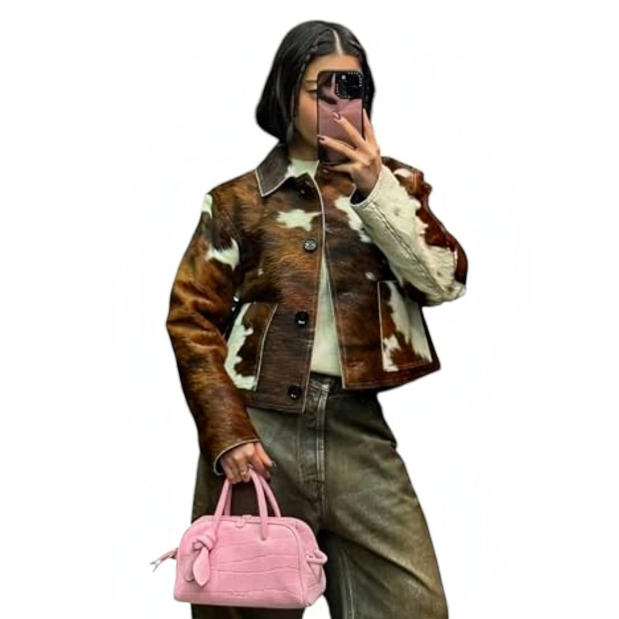 A woman takes a mirror selfie wearing a brown and white cow-print cropped jacket with a cream collar and cuffs, paired with olive green jeans and holding a pink handbag.