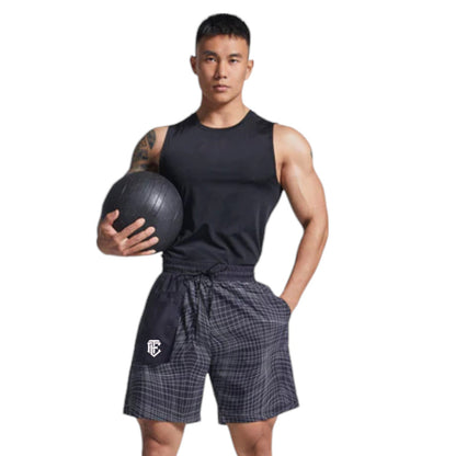 Man holding a medicine ball wearing a black tank top and checkered shorts on a white background