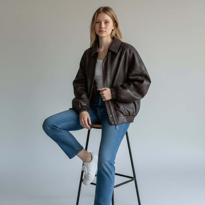 Fit to lead Traders brown genuine leather bomber jacket with ribbed cuffs and hem, worn by a woman with jeans and white sneakers.